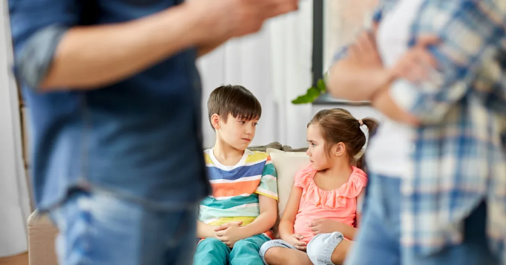 Two young children on a sofa watching their parents argue in the foreground