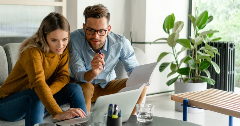 Young couple on a sofa reviewing paperwork together on a laptop