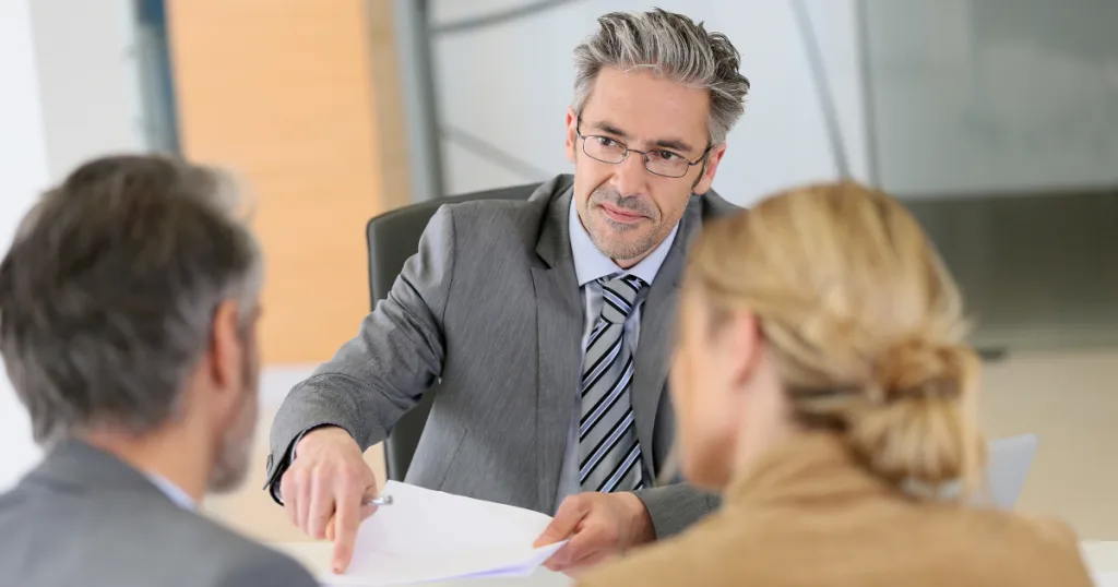 Attorney in a gray suit reviewing paperwork with a couple across his desk
