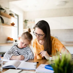 Mother in glasses helping her young daughter with homework at the kitchen table