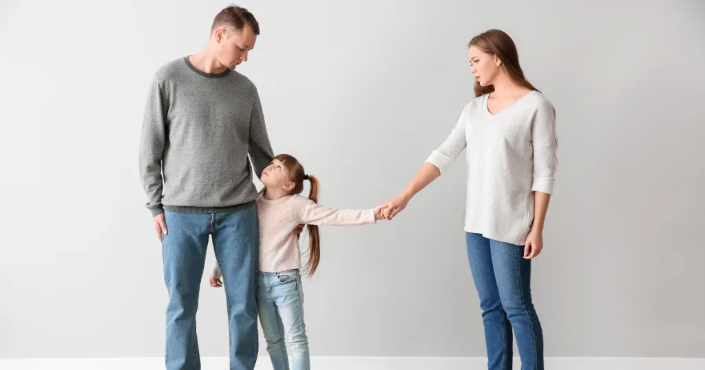 Young girl standing between separated parents, holding her mother's hand and looking up at her father