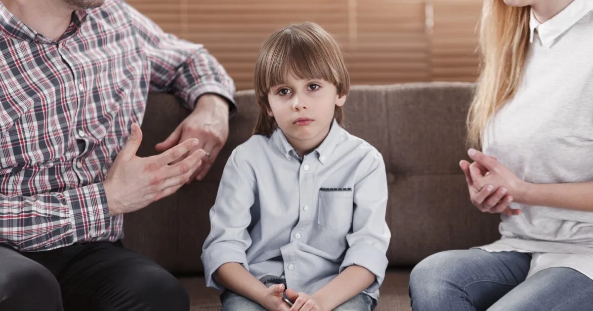 Sad young boy sitting on a couch between his parents as they talk