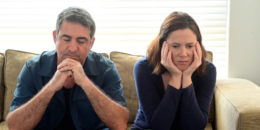 Unhappy couple sitting apart on a couch, both lost in thought